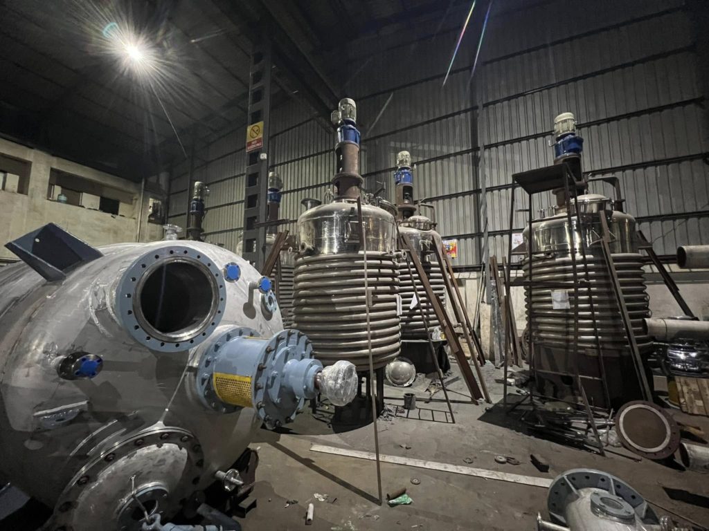 Assembly area at Raviraj Engineering with multiple stainless steel reactor vessels and process equipment.